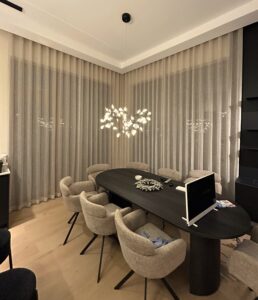 Avar ja valgusküllane kontoriruum, kus on maast laeni beežid poolpimendavad tekstiilkardinad, mis loovad hubase ja professionaalse miljöö